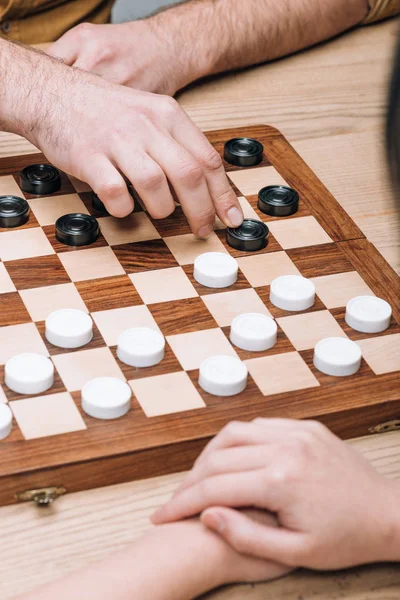 Selective focus of man and woman playing checkers at wooden table — Stock Photo