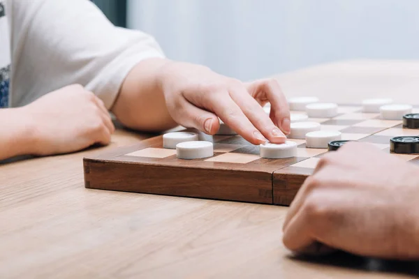 Vista recortada del hombre y la mujer jugando damas en la mesa de madera - foto de stock