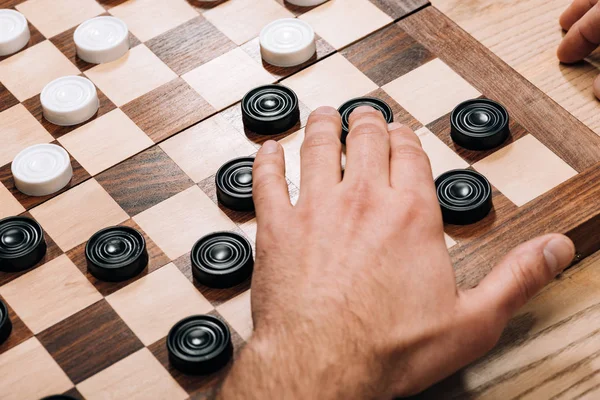 Cropped view of man playing black checkers on chessboard on table — Stock Photo