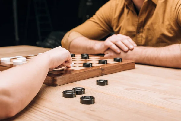 Cropped view of man and woman playing checkers at wooden table — Stock Photo