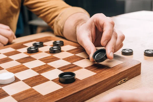 Selective focus of man holding black checker on wooden checkerboard — Stock Photo