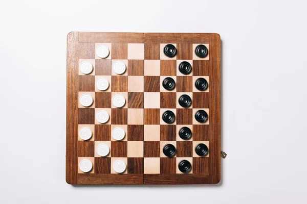 Vista superior de damas en blanco y negro sobre tablero de ajedrez de madera sobre fondo blanco - foto de stock