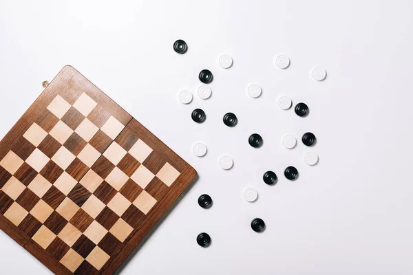 Vista superior de damas por tablero de ajedrez de madera sobre fondo blanco - foto de stock