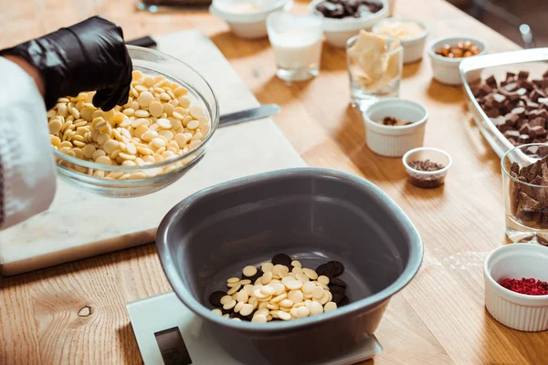 Vista cortada de chocolatier adicionando chips de chocolate branco em tigela em escalas de cozinha — Fotografia de Stock