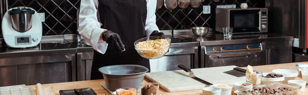 Colpo panoramico di cioccolatiere aggiungendo gocce di cioccolato bianco in ciotola su bilance da cucina — Foto stock