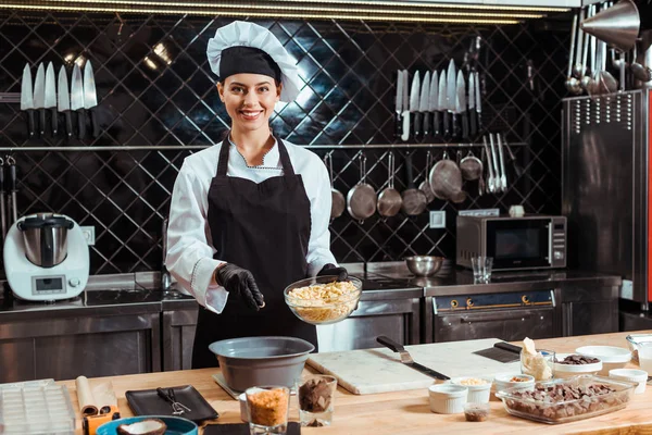 Happy chocolatier in apron adding white chocolate chips into bowl — Stock Photo
