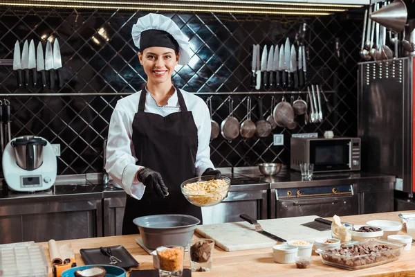 Glücklich Chocolatier in Schürze hinzufügen weiße Schokolade Chips in Schüssel — Stockfoto