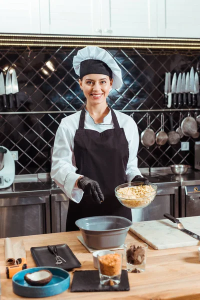 Chocolatier alegre em avental adicionando chips de chocolate branco em tigela — Fotografia de Stock