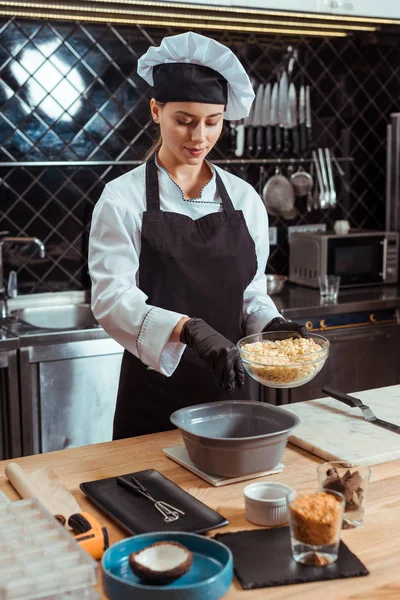 Atraente chocolatier no avental adicionando chips de chocolate branco em tigela — Fotografia de Stock