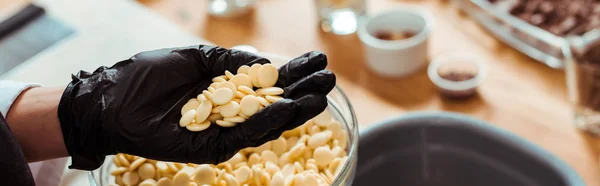 Panoramic shot of chocolatier holding white chocolate chips in hand — Stock Photo