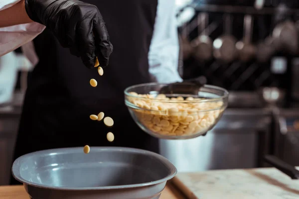 Cropped view of chocolatier adding white chocolate chips into bowl in kitchen — Stock Photo