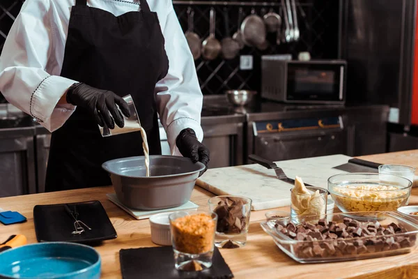 Vista recortada de chocolatero verter leche en un tazón — Stock Photo