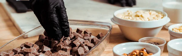 Panoramic shot of chocolatier in black latex glove taking dark chocolate cubes — Stock Photo