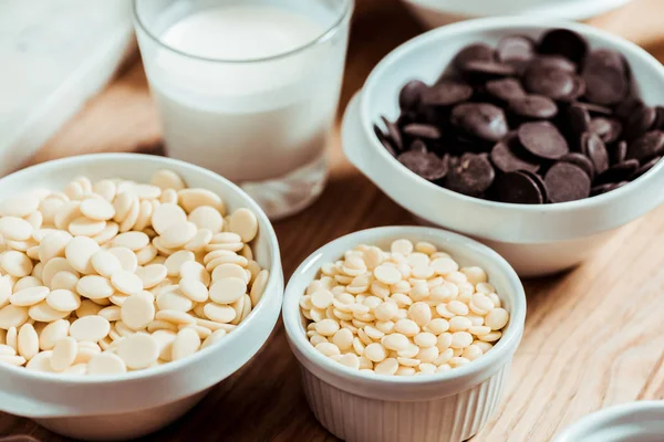 Selective focus of white chocolate chips in bowls near glass with milk — Stock Photo