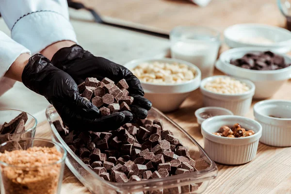 Vista recortada de la mujer en guantes de látex negro con cubos de chocolate - foto de stock