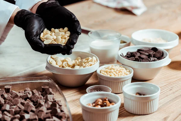Foco seletivo de chocolate em luvas de látex preto segurando chips de chocolate branco — Fotografia de Stock