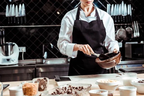 Cropped view of chocolatier in apron holding silicone spatula while mixing chocolate in bowl — Stock Photo