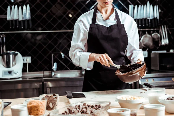 Vista cortada de chocolatier em avental segurando espátula de silicone ao misturar chocolate em tigela — Fotografia de Stock