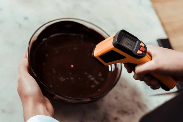 Ausgeschnittene Ansicht des Chocolatiers, der das Kochthermometer in der Nähe der Schüssel mit dunkler Schokolade hält — Stockfoto