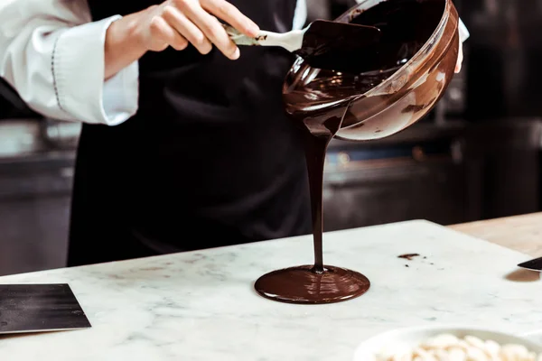 Обрезанный вид на шоколадную глазурь, льющую расплавленный шоколад на мраморную поверхность — стоковое фото
