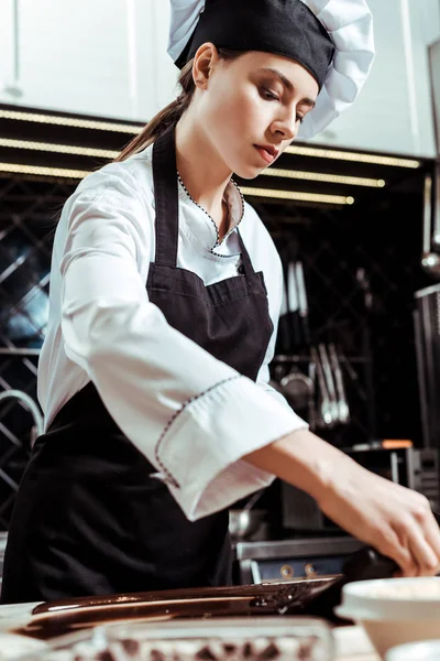 Attraente cioccolatiere tenendo raschietto torta vicino cioccolato fondente fuso — Foto stock