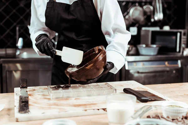 Cropped view of chocolatier in apron pouring melted chocolate into ice tray — Stock Photo