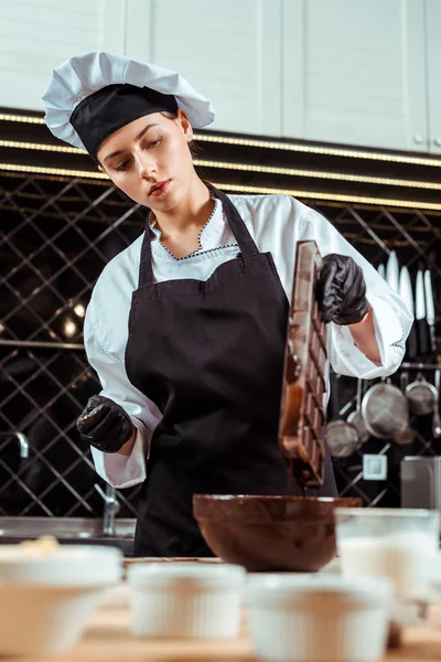 Foco seletivo de chocolate no avental segurando bandeja de gelo com chocolate derretido perto da tigela — Fotografia de Stock