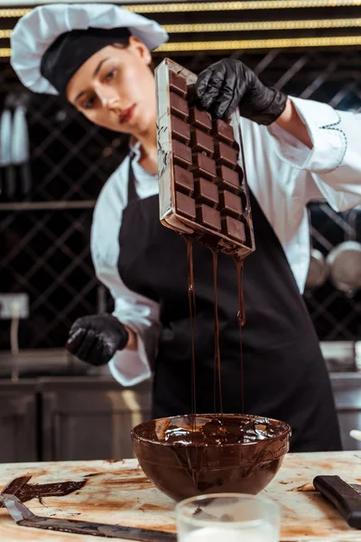 Selective focus of attractive chocolatier in apron holding ice tray with melted chocolate near bowl — Stock Photo