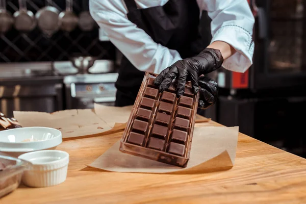 Vue recadrée du chocolatier tenant un plateau de glace avec du chocolat près du papier cuisson — Photo de stock