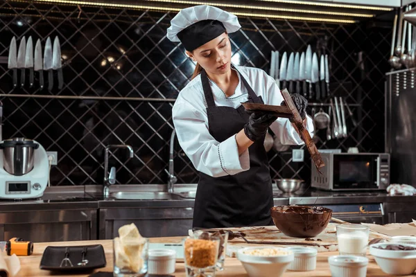 Attraktive Chocolatier halten Kuchen glättet in der Nähe Schüssel mit Schokolade — Stockfoto