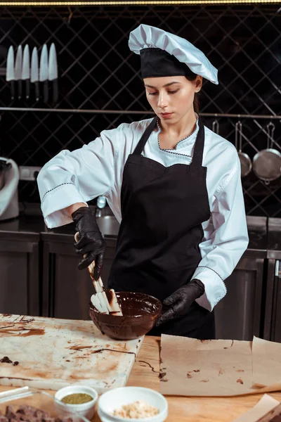 Attractive chocolatier holding silicone spatula near bowl with melted chocolate in kitchen — Stock Photo