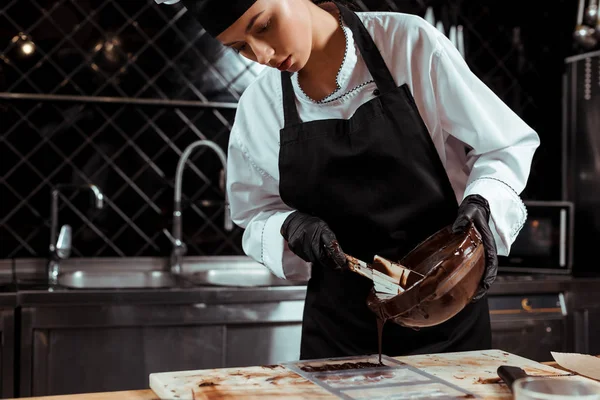 Bonito chocolatier derramando chocolate derretido na superfície de mármore — Fotografia de Stock