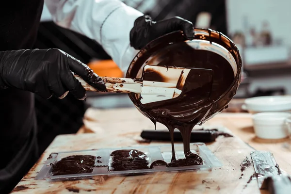 Vista cortada de chocolatier derramando chocolate derretido em moldes de chocolate — Fotografia de Stock