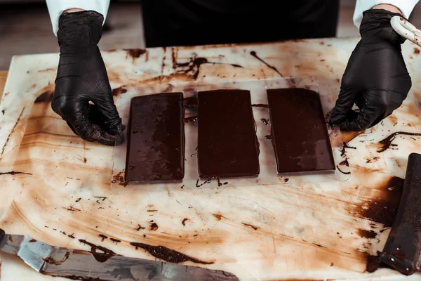 Ausgeschnittene Ansicht eines Chocolatiers in Latexhandschuhen in der Nähe von Schokoriegeln — Stockfoto