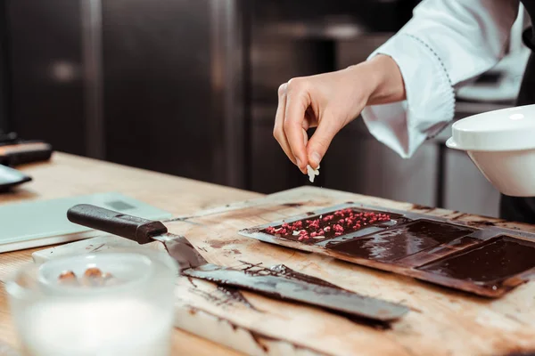 Vue recadrée du chocolatier ajoutant des flocons de noix de coco sur la barre de chocolat noir — Photo de stock