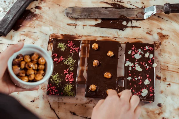 Vista dall'alto del cioccolatiere aggiungendo nocciole caramellate nella barretta di cioccolato fondente — Foto stock