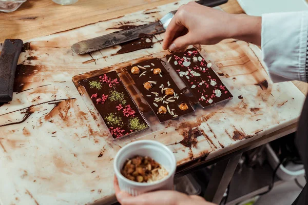 Vista ritagliata di cioccolatiere aggiungendo noci in barretta di cioccolato fondente — Foto stock