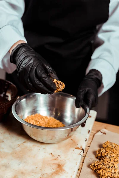 Cropped view of chocolatier in black latex gloves holding delicious candy with flakes — Stock Photo