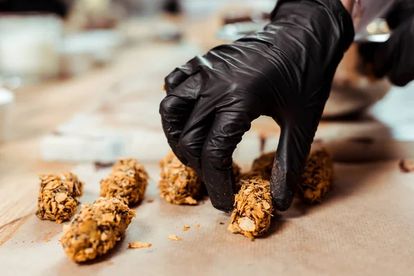 Cropped view of chocolatier in black latex glove taking delicious chocolate candy with flakes — Stock Photo