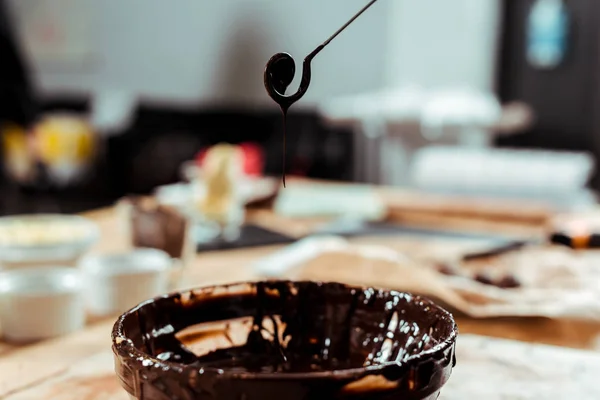 Foco seletivo de redemoinho batedor com gotas de chocolate derretido perto tigela — Fotografia de Stock
