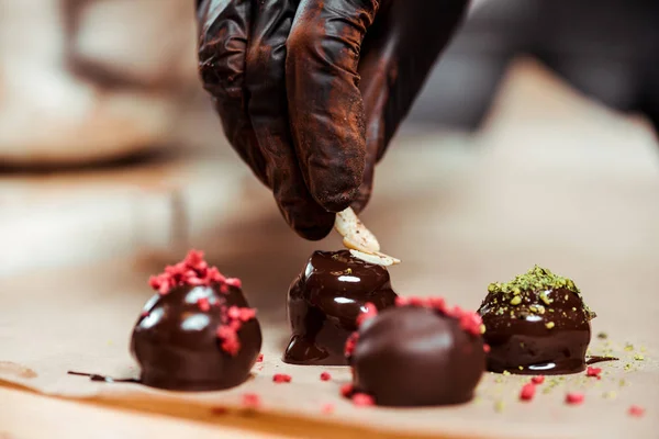 Vista cortada de chocolate em luva de látex preto adicionando nozes em doces frescos — Fotografia de Stock