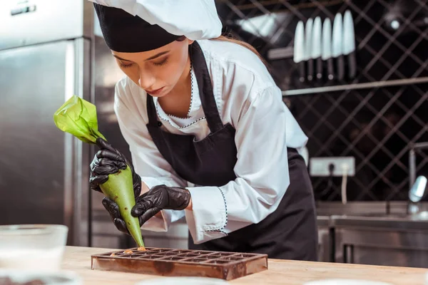 Selective focus of attractive chocolatier in black latex gloves holding pastry bag near chocolate molds — Stock Photo