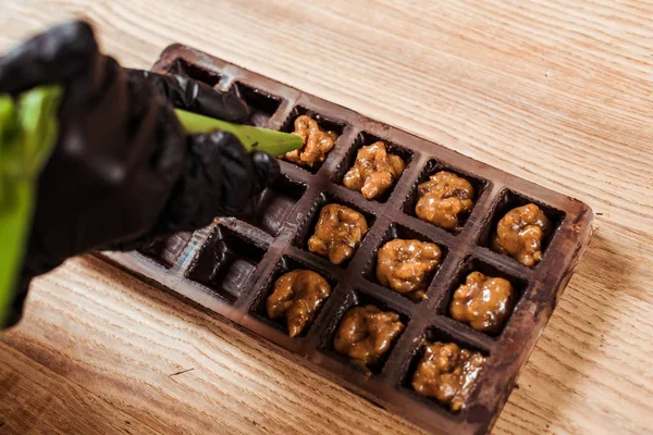 Cropped view of chocolatier in latex gloves holding pastry bag with caramelized nuts near chocolate molds — Stock Photo