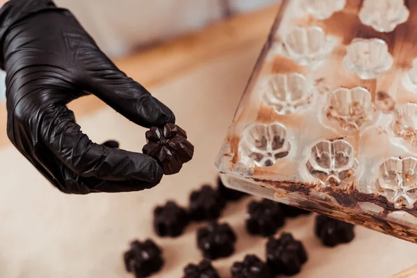 Close up of chocolatier holding chocolate candy near chocolate molds — Stock Photo