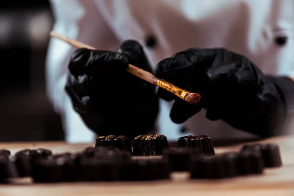 Vista ritagliata di cioccolatiere pennello vicino caramelle al cioccolato — Foto stock