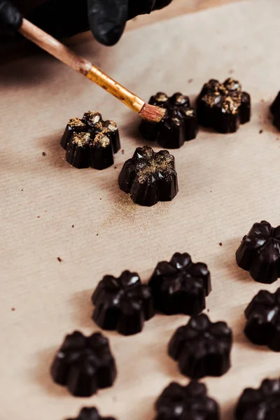 Abgeschnittene Ansicht des Chocolatiers, der Pinsel mit Goldpuder in der Nähe von zubereiteten Schokoladenbonbons hält — Stockfoto