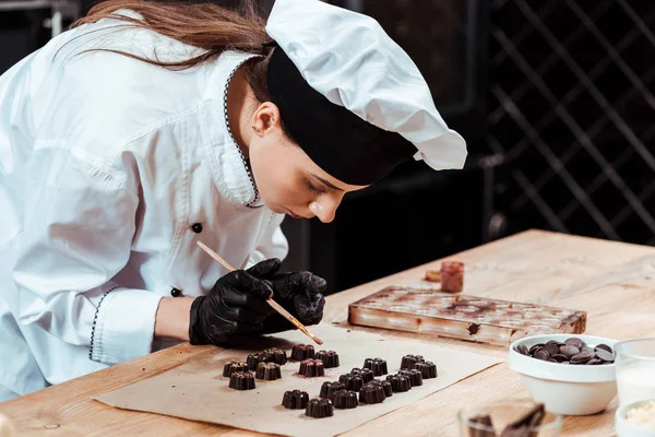 Atraente Chocolatier segurando escova com pó de ouro perto de doces de chocolate preparados — Fotografia de Stock