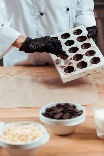 Vue recadrée du chocolatier tenant des bonbons savoureux et un plateau de glace avec des bonbons au chocolat congelés — Photo de stock