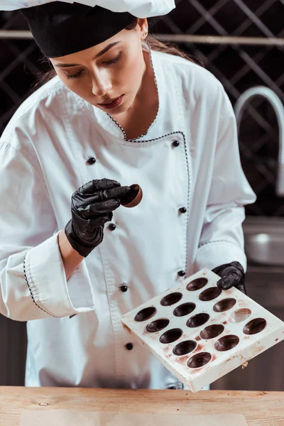 Attrayant chocolatier regardant des bonbons savoureux et tenant des moules de chocolat — Photo de stock