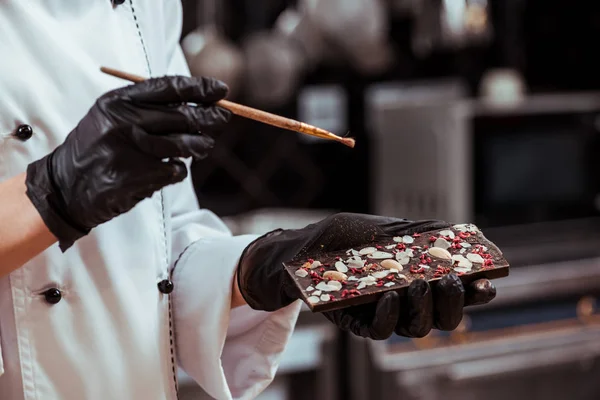 Cropped view of chocolatier holding chocolate bar and brush — Stock Photo